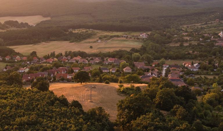 Panorámakép Kóspallag településről, erdőkkel övezett dombvidéki tájban.